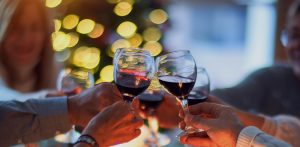 five hands toasting wine glasses with red wine with lights in blurred background